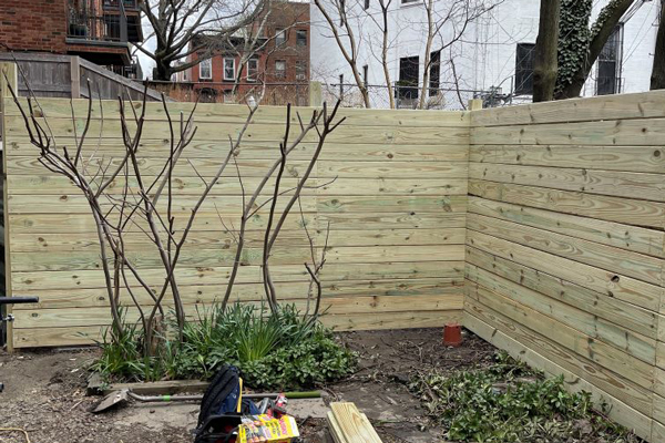 A wooden fence is under construction in a backyard, showcasing the process of building a sturdy outdoor barrier.